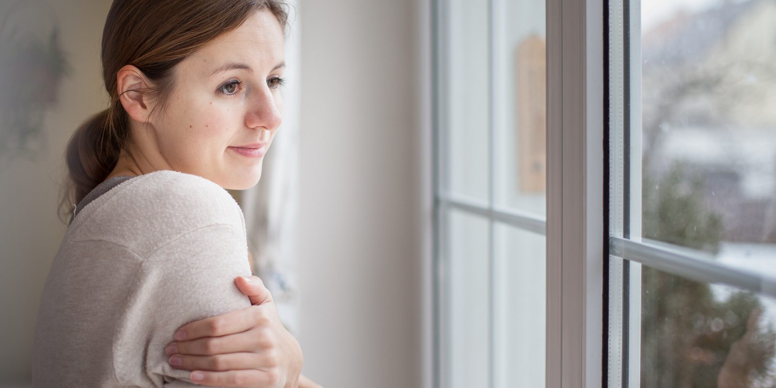 Woman looking from a window of her house on a cold and snowy winter day