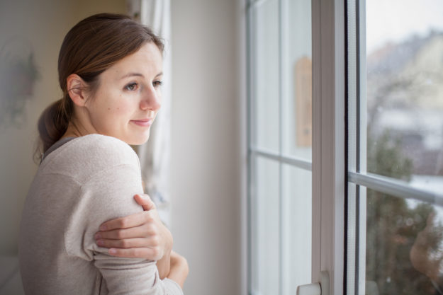 Energy Saving Tips for your Home this Winter Woman looking from a window of her house on a cold and snowy winter day