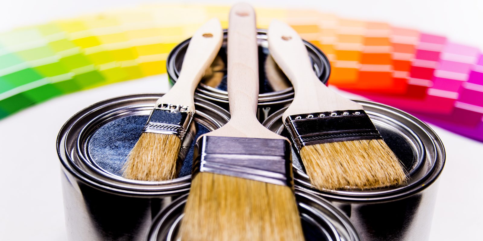 Painting brushes, paint cans, paint samples, paint concept, paint inside cans with paint color samples in background, yellow paint, white paint, red peint, three cans of different paint, paint samples from pink paint to dark blue paint