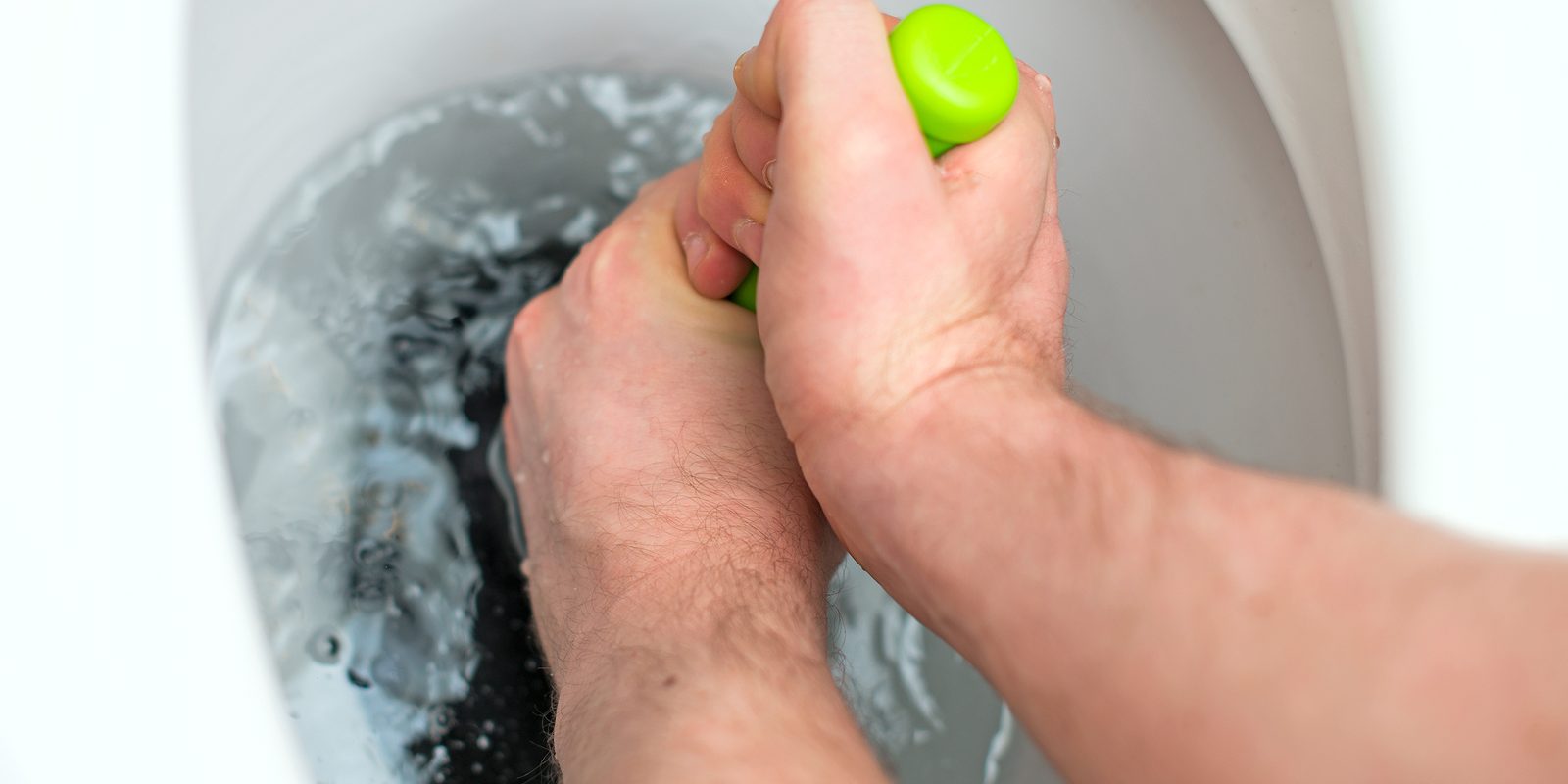 Plumber repairing toilet with a hand plunger.