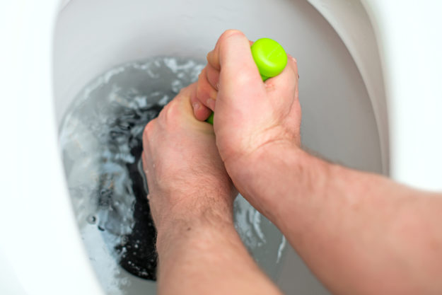 Never Flush These Items Plumber repairing toilet with a hand plunger.