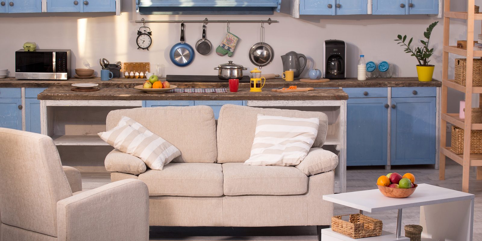 Close up view on kitchen studio. Living room with small sofa, chair and coffe table with kitchen on background.