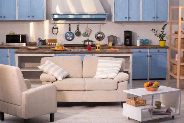 small-spaces Close up view on kitchen studio. Living room with small sofa, chair and coffe table with kitchen on background.